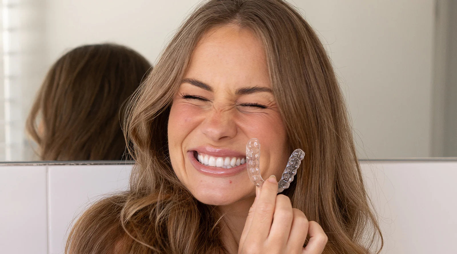 Woman holding a clear dental aligner in front of her face