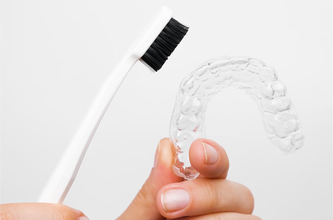 Clear aligner held by a hand with a tooth brush and a white background