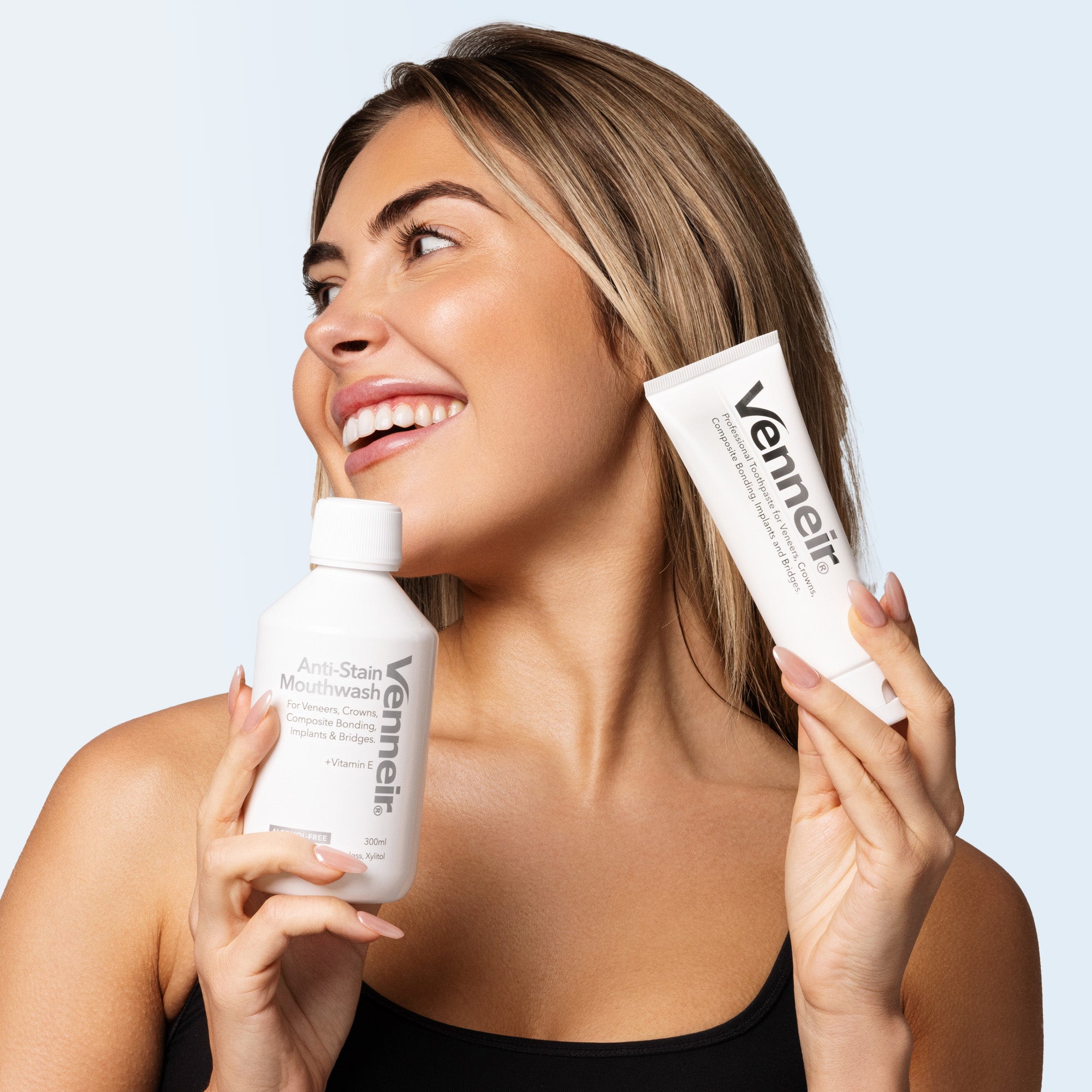 Woman holding Venneir mouthwash and tube against a light blue background
