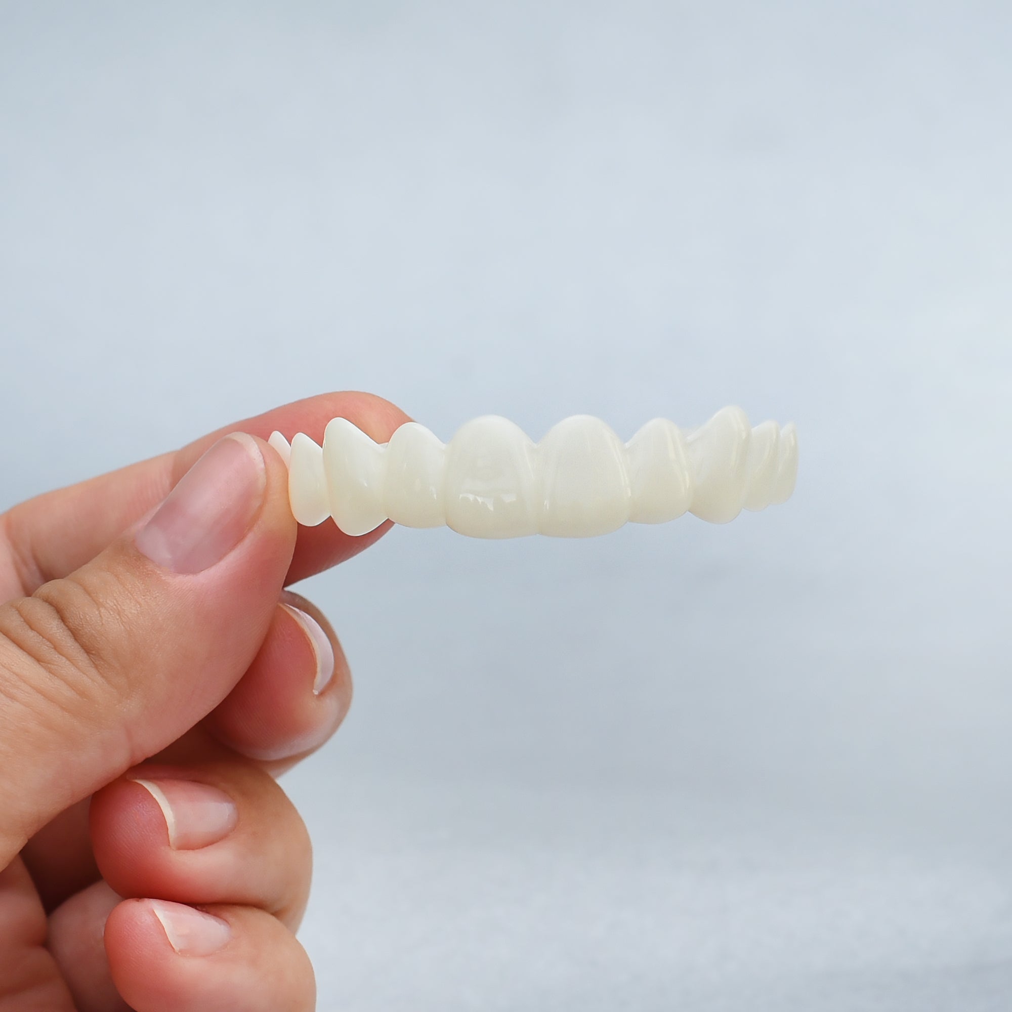 Hand holding a white snap on smile against a light blue background