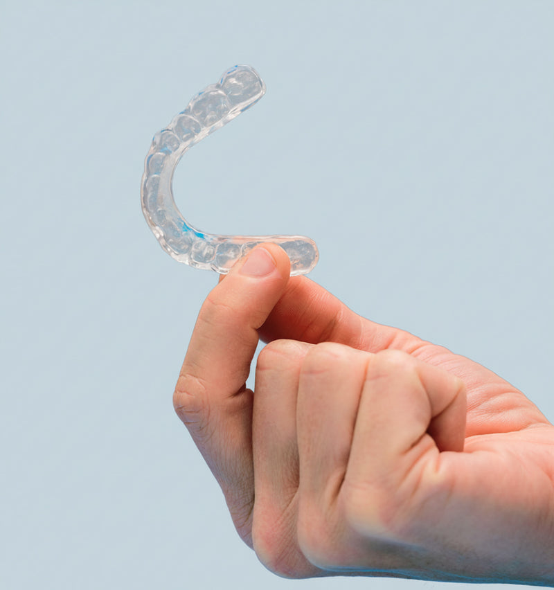 Hand holding a clear night guard against a light blue background