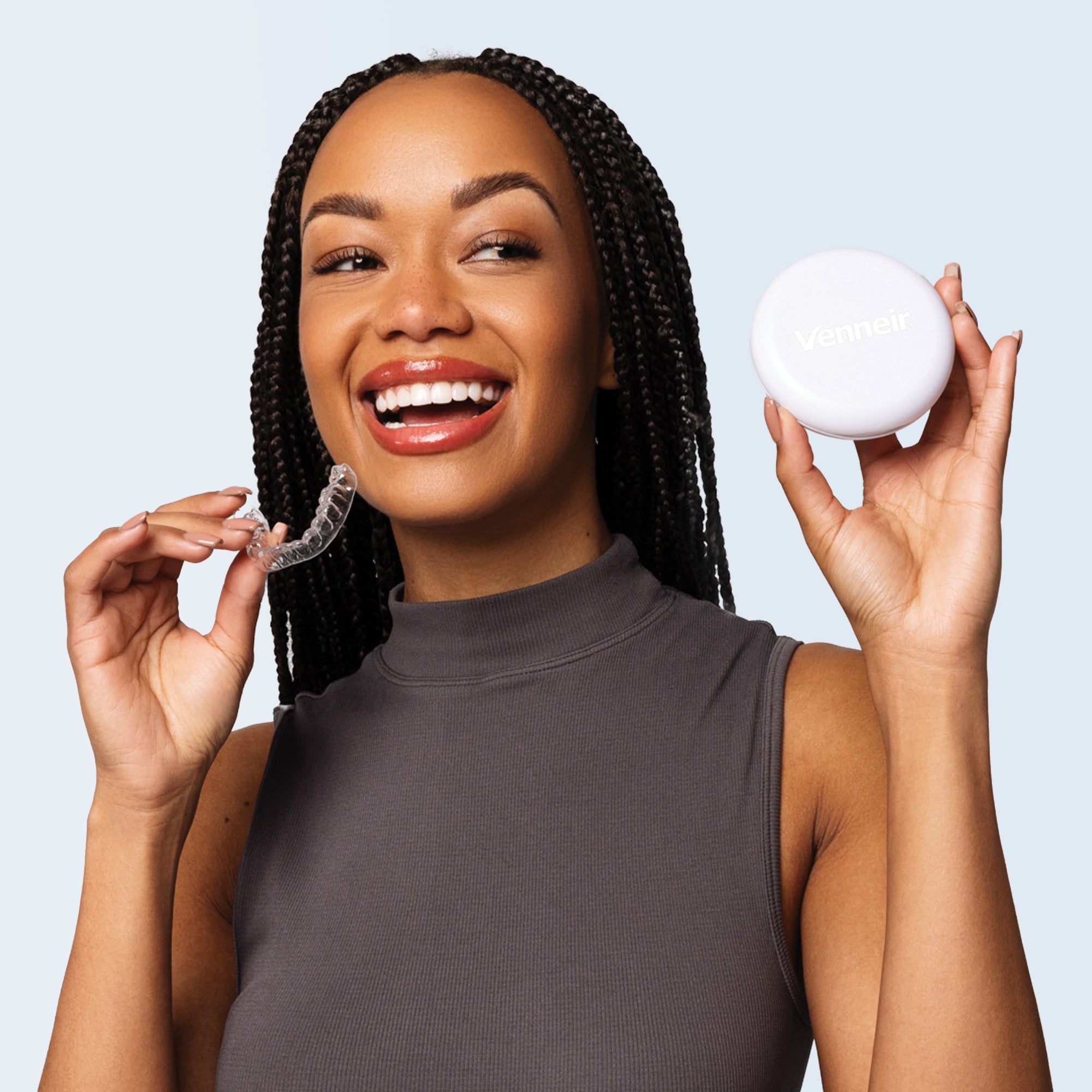 Woman holding a clear dental aligner and a white storage case against a light blue background