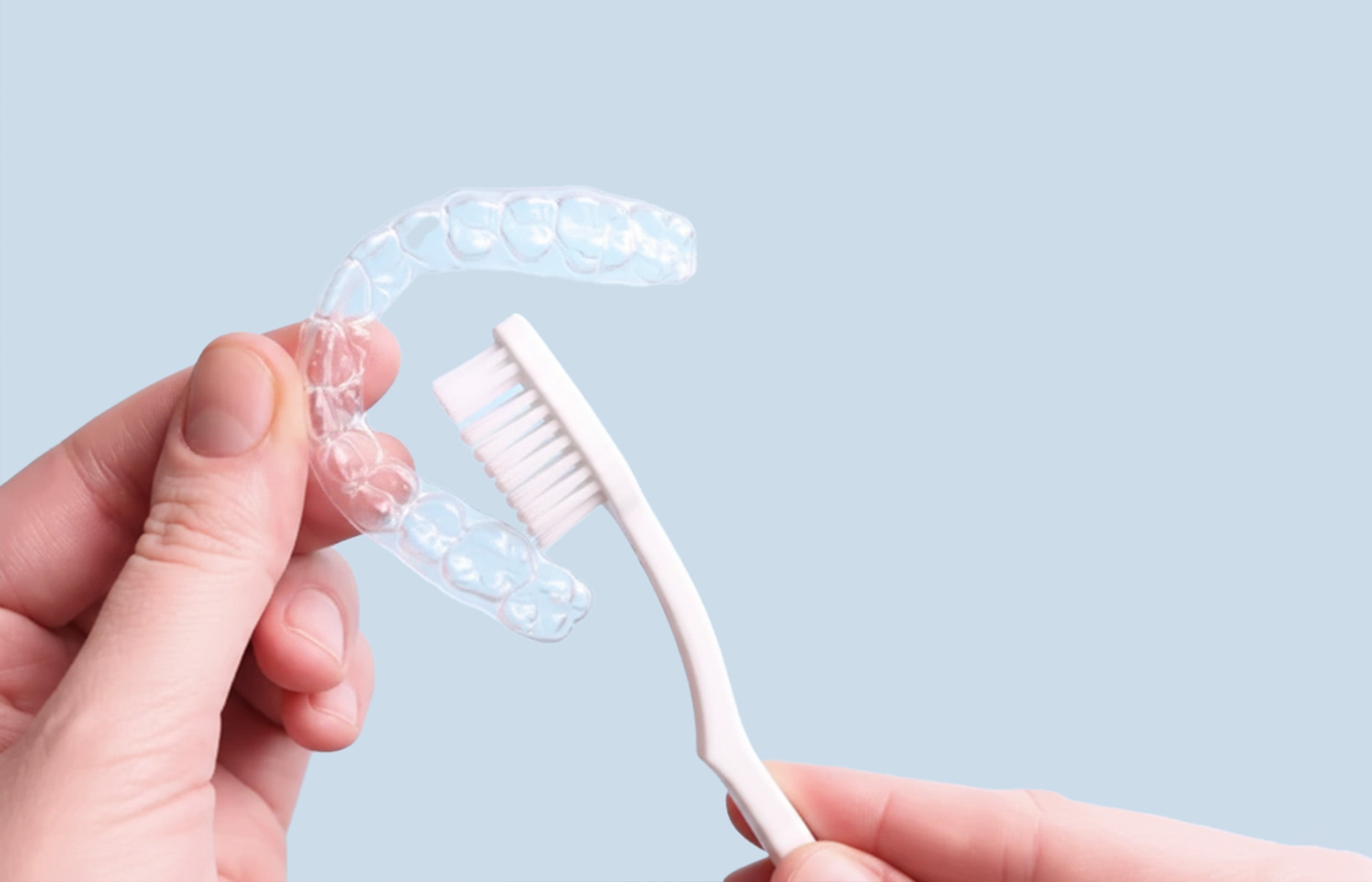 Hands cleaning a retainer or aligner with toothbrush