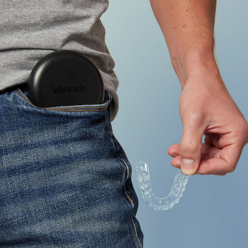 Person holding a clear mouthguard with a retainer case in their pocket against a light blue background