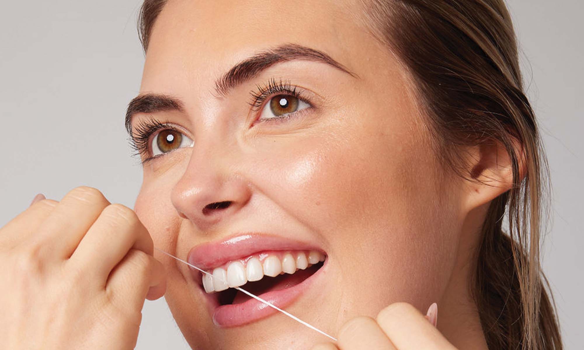 Woman using dental floss with a plain background