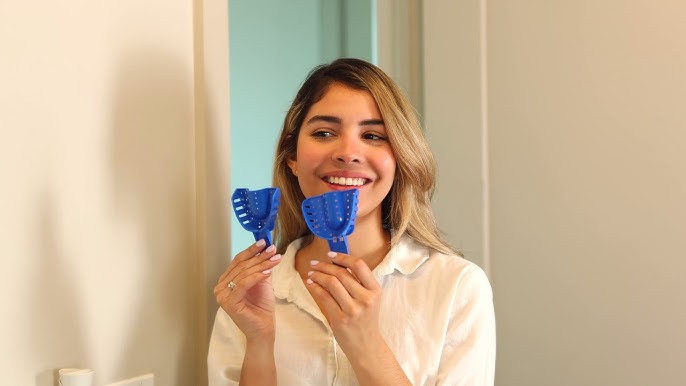 Woman holding two blue silicone impressions in front of a mirror