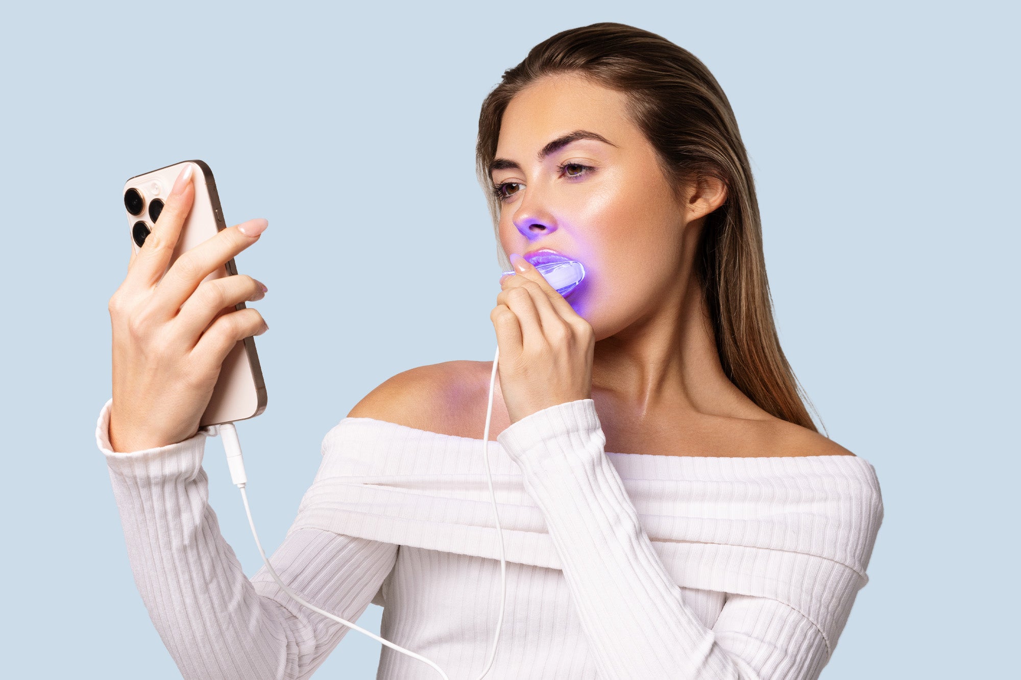Woman using a LED whitening light with a phone on a light blue background