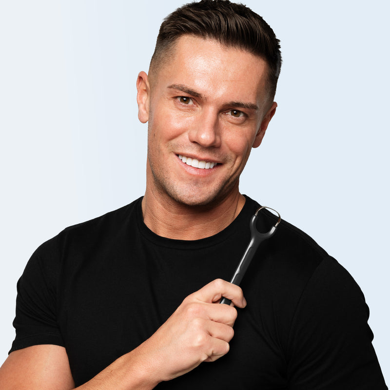 Man holding a tongue scraper against a light gray background