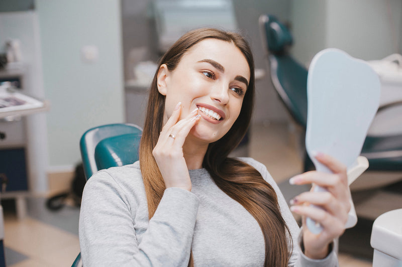 Woman examining her smile in a mirror at a dental office
