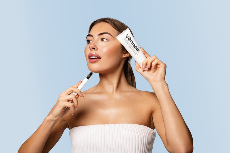 Woman holding toothbrush and toothpaste with Venneir branding and blue background