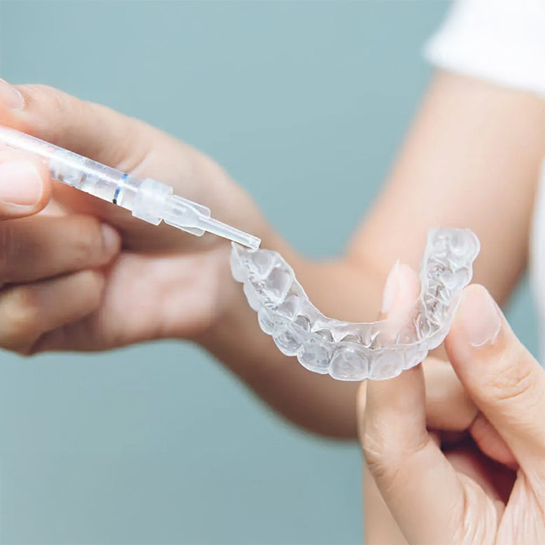 Woman applying whitening gel to clear upper and lower whitening trays on light blue background